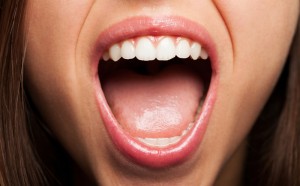 A close-up view of a woman who is smiling big with her mouth open, revealing her tongue.