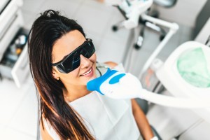 A brunette woman wearing glasses in a dental chair as she is about to receive a professional teeth whitening treatment.